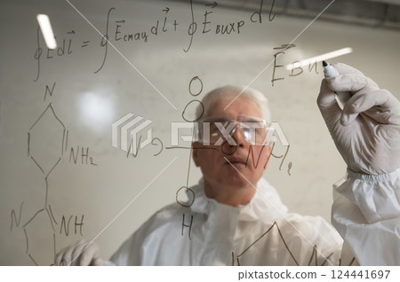 An elderly Caucasian male chemist in a protective suit writes on glass. An elderly Caucasian male chemist in a protective suit writes on glass. 124441697