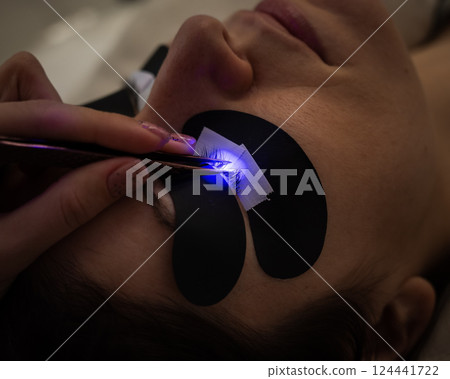 A woman undergoing eyelash extension procedure using an ultraviolet lamp. A woman undergoing eyelash extension procedure using an ultraviolet lamp. 124441722