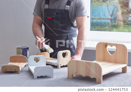 Men's hands painting baby wooden doll cots. 124441753