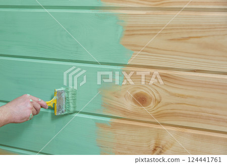 hand paints a wooden vertical surface with green paint. 124441761