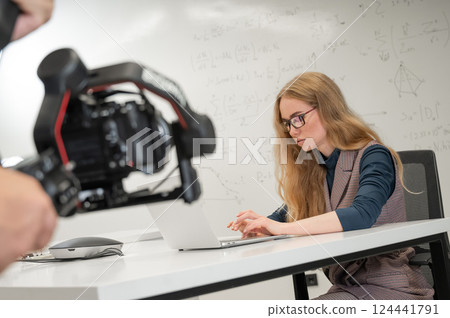 Caucasian female scientist typing on laptop. White board with formulas. Photo shoot. Caucasian female scientist typing on laptop. White board with formulas. Photo shoot. 124441791
