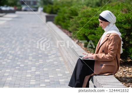Portrait of young woman in hijab using laptop outdoors. Portrait of young woman in hijab using laptop outdoors. 124441832