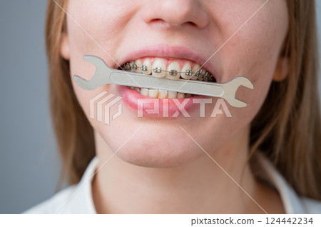 Close-up portrait of a woman with braces holding a wrench in her teeth. Close-up portrait of a woman with braces holding a wrench in her teeth. 124442234