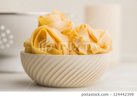 Italian pasta tagliatelle. Uncooked noodle pasta in bowl on kitchen table. 124442399