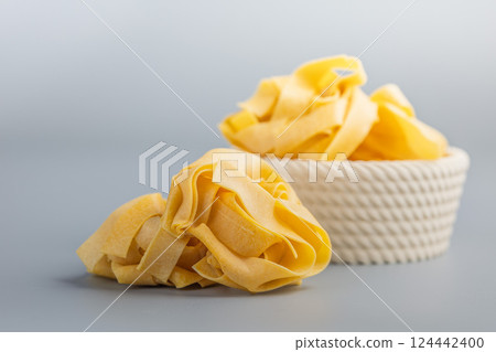 Italian pasta tagliatelle. Uncooked noodle pasta on grey background. 124442400