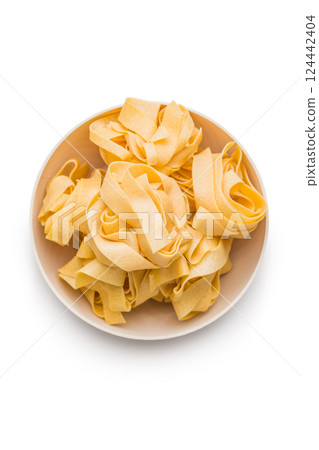 Italian pasta tagliatelle. Uncooked noodle pasta in bowl isolated on white background. Italian pasta tagliatelle. Uncooked noodle pasta in bowl isolated on white background. 124442404