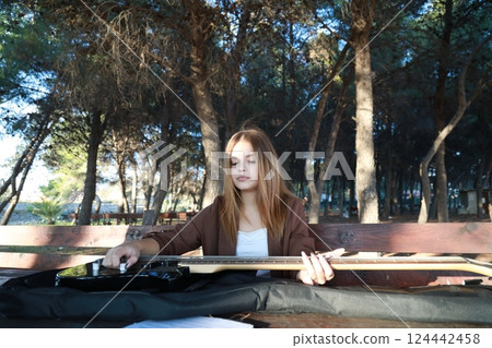 Girl Plays Bass Musical Instrument Sitting In Table In The Mountain Forest Girl Plays Bass Musical Instrument Sitting In Table In The Mountain Forest 124442458