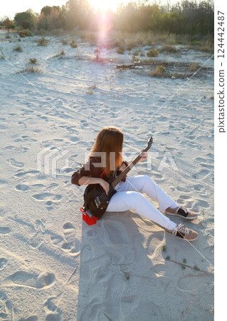 Girl Plays The Bass Instrument Sitting On The Beach At Sunset Near The Ocean 124442487