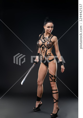 Woman poses confidently in lingerie with body art and sword in dark setting 124442537