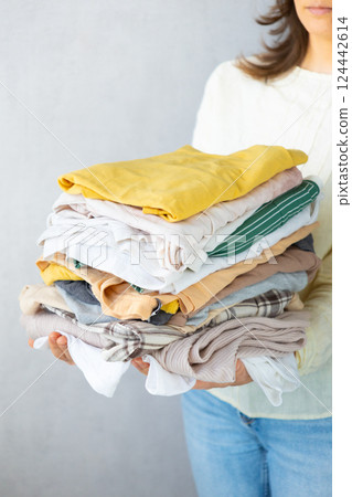 Laundry, woman holds stack of clothes in her hands after dry cleaning. housework, cleaning ironing. Laundry, woman holds stack of clothes in her hands after dry cleaning. housework, cleaning ironing. 124442614