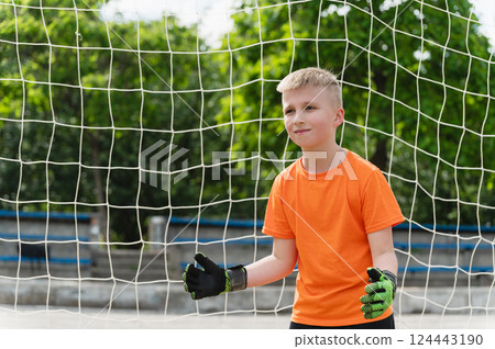 Boy in orange t-shirt and green gloves stands ready in goal. 124443190