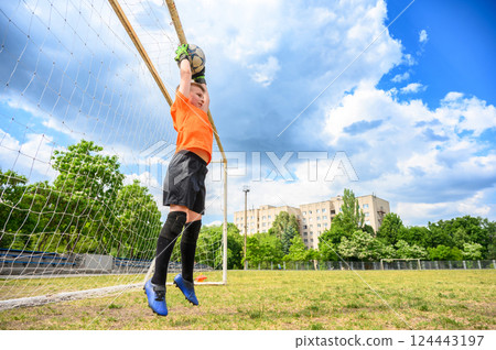 Goalkeeper boy jumping to catch ball near goalpost. Goalkeeper boy jumping to catch ball near goalpost. 124443197
