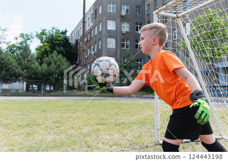 Goalkeeper boy throwing soccer ball into play outdoors. 124443198