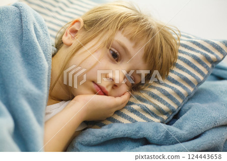 Tired child lying in bed on a pillow. Adorable little girl indoor portrait Tired child lying in bed on a pillow. Adorable little girl indoor portrait 124443658