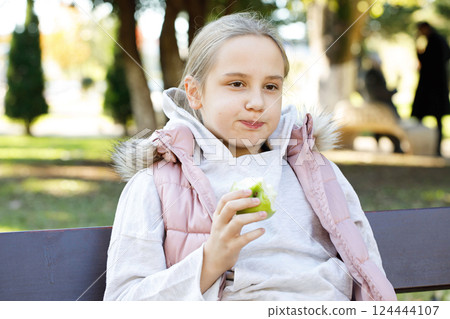 Pretty child eating apple fruit outdoors. Young girl 10 years old 124444107