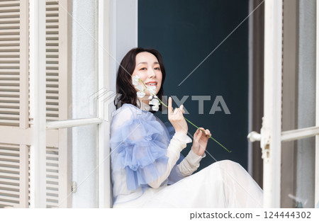 Woman with flowers by the window Woman with flowers by the window 124444302