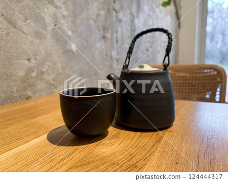 Black ceramic teapot with cup on wooden table in cozy cafe interior. Calm, ritual, and mindful tea drinking experience 124444317