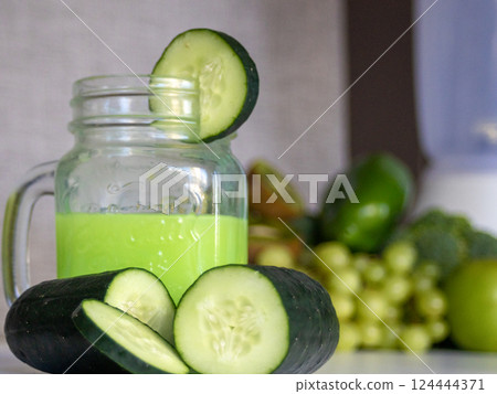 Green juice of cucumbers and fresh fruits on blurred background. 124444371