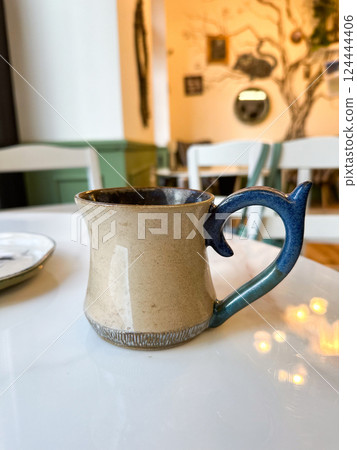 Artisan coffee mug on white marble table in cozy cafe. Calm, presence, and the simple beauty of daily rituals and handmade design Artisan coffee mug on white marble table in cozy cafe. Calm, presence, and the simple beauty of daily rituals and handmade design 124444406