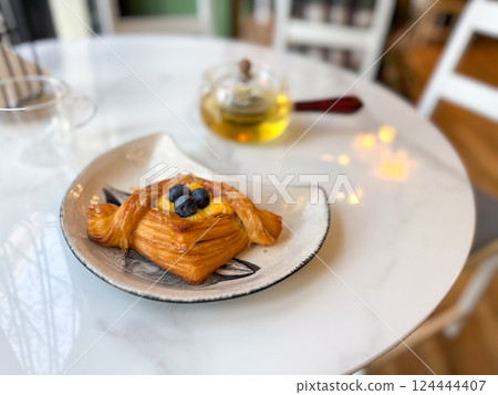 Blueberry pastry with tea served on white marble table. Represents comfort, calm, and sweet daily rituals in a cozy cafe atmosphere 124444407
