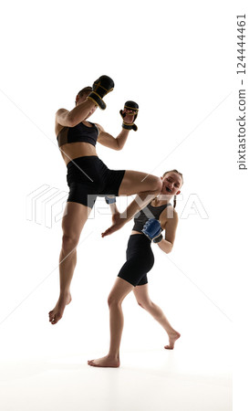 One female athlete lands knee strike to opponent body while sparring in intense training session isolated on white background. One female athlete lands knee strike to opponent body while sparring in intense training session isolated on white background. 124444461