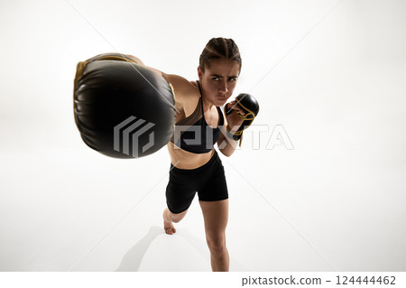 Powerful punch from female fighter in boxing gloves directed toward camera with intense expression and focus. 124444462