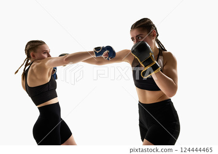 Two athletic women engaged in sparring, throwing punches in close range combat wearing gloves and sportswear. Two athletic women engaged in sparring, throwing punches in close range combat wearing gloves and sportswear. 124444465