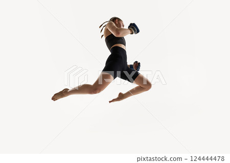 Low angle view of woman captured in high jump with boxing gloves, fierce focus training against white background. Low angle view of woman captured in high jump with boxing gloves, fierce focus training against white background. 124444478