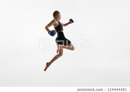 Woman with braids captured in high jump with boxing gloves, fierce focus training against white background. 124444481