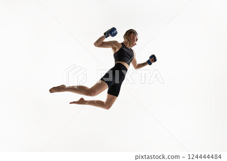 Powerful female fighter in mid-air pose with clenched fists ready to strike, frozen in motion against white background. Powerful female fighter in mid-air pose with clenched fists ready to strike, frozen in motion against white background. 124444484