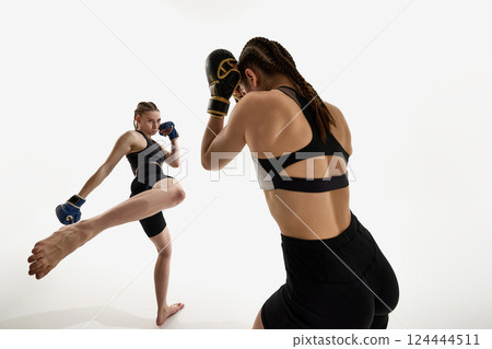 Intense moment of MMA combat between two athletic women mid-strike against white background. 124444511