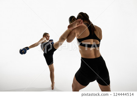 Focused young woman delivering high kick during martial arts match against white background. 124444514