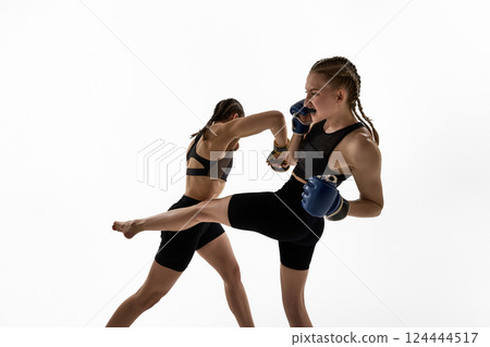 Women in boxing gloves performing high kick and punch during sparring against white studio background 124444517