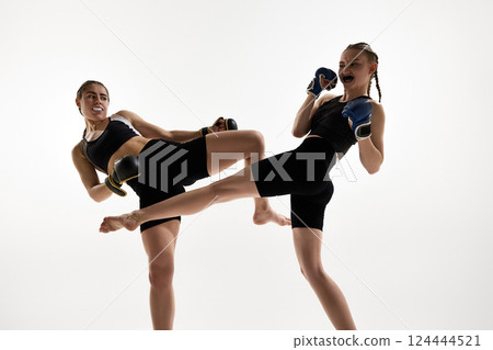 Close-up of female martial artists mid-kick with focused faces and protective mouth guards training against white background 124444521