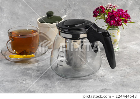 Glass teapot with metal strainer inside. Kitchen utensils on gray background. Glass teapot with metal strainer inside. Kitchen utensils on gray background. 124444548