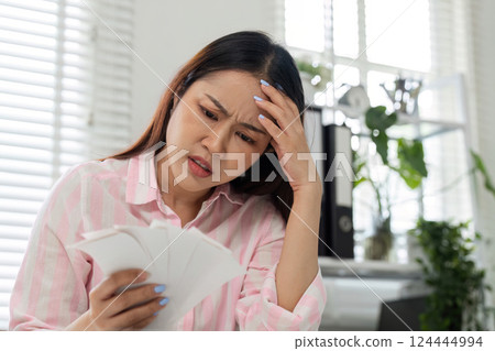 Navigating Financial Anxiety and Home Office Work. A woman appears troubled while looking over her financial documents. Navigating Financial Anxiety and Home Office Work. A woman appears troubled while looking over her financial documents. 124444994