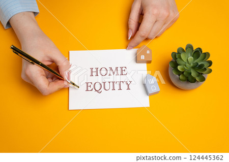Home equity concept. Difference between the current market value of your home and the outstanding balance of any loans or mortgages secured by the property. A woman writes in notes. Real estate 124445362