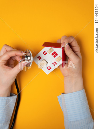 Woman holding stethoscope near small house. Housing condition and maintenance. Apartment renovation. Property valuation. Real estate concept Woman holding stethoscope near small house. Housing condition and maintenance. Apartment renovation. Property valuation. Real estate concept 124445394