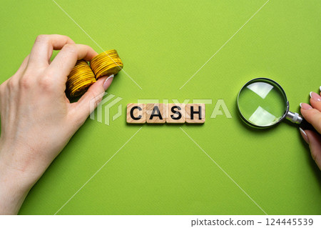 Cash word concept. Physical money in the form of coins and paper bills that is used as a medium of exchange for goods and services. Coins in female hands and magnifying glass. Wooden blocks Cash word concept. Physical money in the form of coins and paper bills that is used as a medium of exchange for goods and services. Coins in female hands and magnifying glass. Wooden blocks 124445539