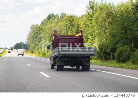 An open flatbed truck drives on a highway in summer. Transportation of goods up to 5 tons. Rental of trucks for regional and international transportation. Copy space for text 124446779