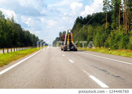 A panel truck with a semi-trailer transports reinforced concrete slabs for building a house. Cargo transportation in summer along the road against the backdrop of the forest. Copy space for text 124446780