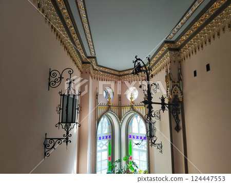 Forged wall lamps in an antique room with patterns on the ceiling and multi-colored windows, interior 124447553