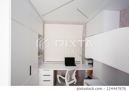 Modern workplace with laptop, computer chair and table in children's bedroom. White furniture and roller blinds on the window. 124447676