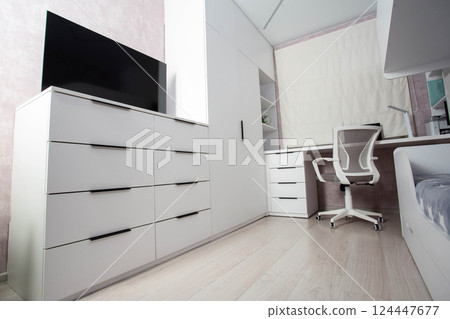 Modern workplace in the bedroom with white furniture, computer desk and chair. The TV is on a white chest of drawers. Bedroom interior. Modern workplace in the bedroom with white furniture, computer desk and chair. The TV is on a white chest of drawers. Bedroom interior. 124447677