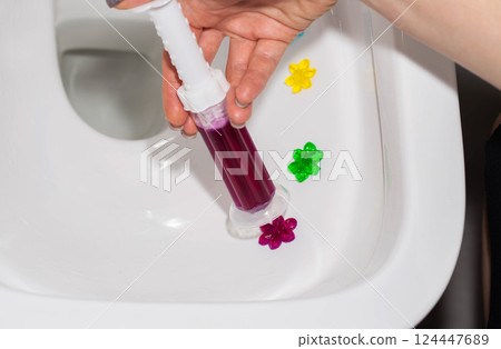 Burgundy gel in a syringe in a hand in the toilet bowl of a toilet in the form of flowers. Antibacterial and disinfectant effect, close-up. Copy space for text 124447689