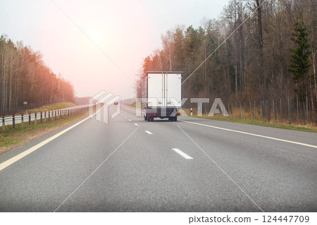 a manufactured goods van transports non-food cargo along a highway in the spring against the backdrop of the sun. Copy space for text, industry a manufactured goods van transports non-food cargo along a highway in the spring against the backdrop of the sun. Copy space for text, industry 124447709