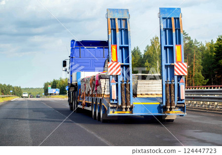 A modern blue tractor with a semi-trailer trawl transports cargo along the highway in the summer, industry. Copy space for text. Trawl trailer service and rental 124447723