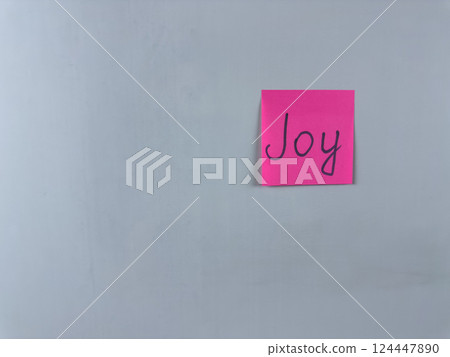 Sticky note with Joy written on it, affixed to a white background. Photo represents happiness and delight, ideal for themes of joy and positive emotions 124447890