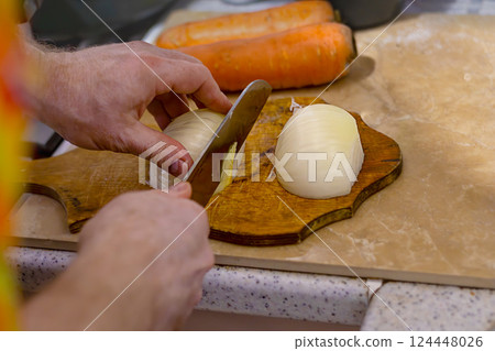 Men's hands slicing onions on wooden board in kitchen. Cooking with fresh vegetables. Healthy eating. Close-up Men's hands slicing onions on wooden board in kitchen. Cooking with fresh vegetables. Healthy eating. Close-up 124448026