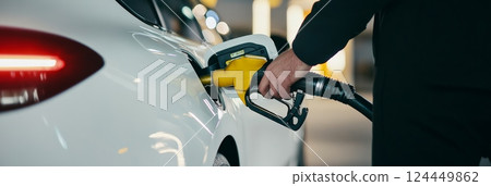 Close up of a driver's hand refueling a white car at a gas station, emphasizing the rising cost of fuel and the importance of efficient energy consumption 124449862